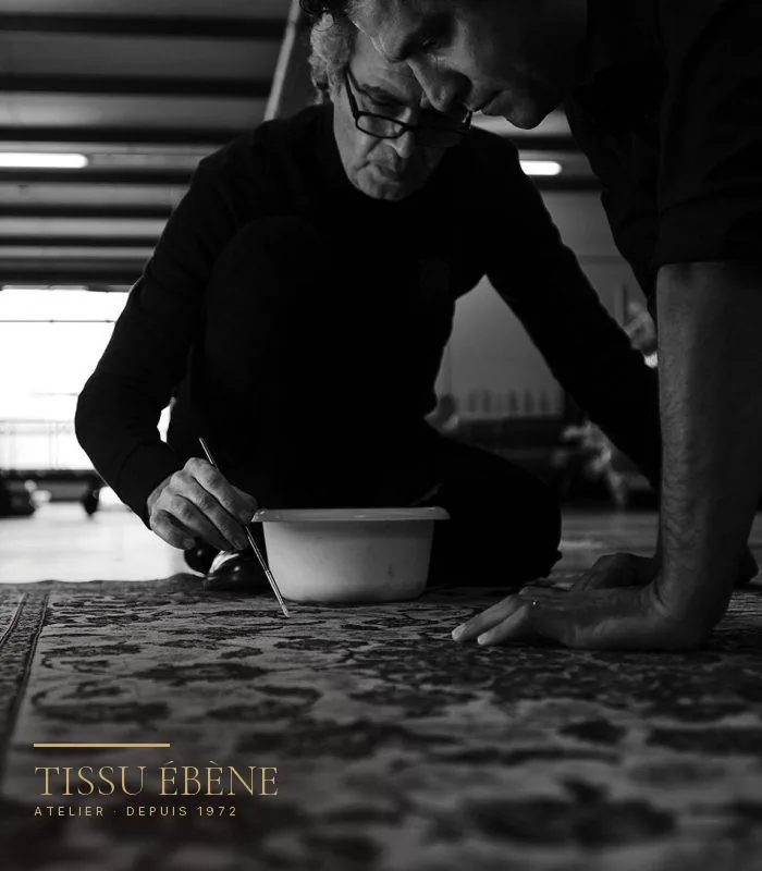 Deux artisans agenouillés sur un tapis, l'un retouchant les couleurs au pinceau fin