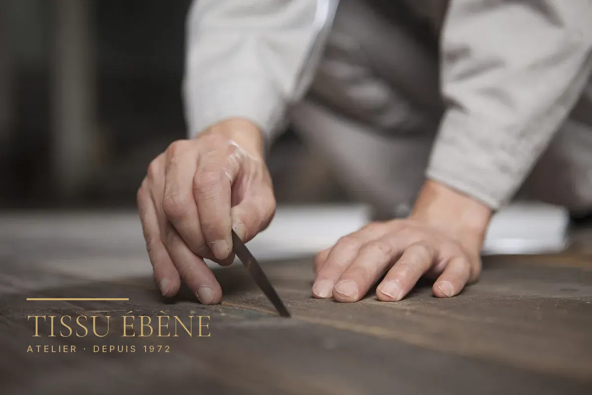 Mains d’artisan guidant un ciseau à bois sur un plateau de bois sombre, gros plan à l’atelier