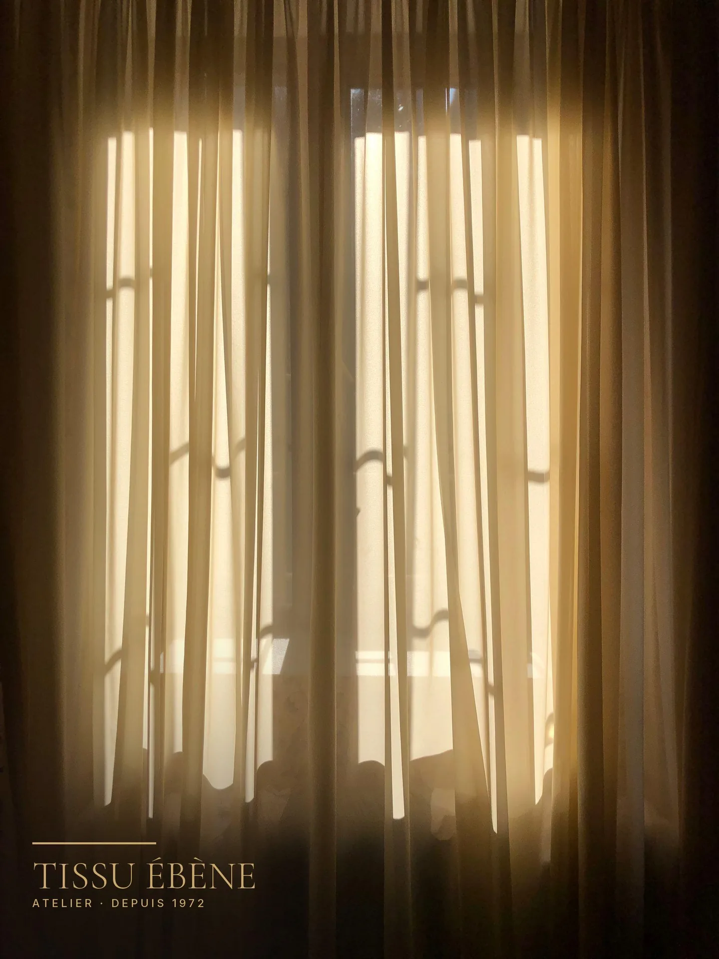 Voilages beiges en contre-jour devant une fenêtre baignée de lumière dorée