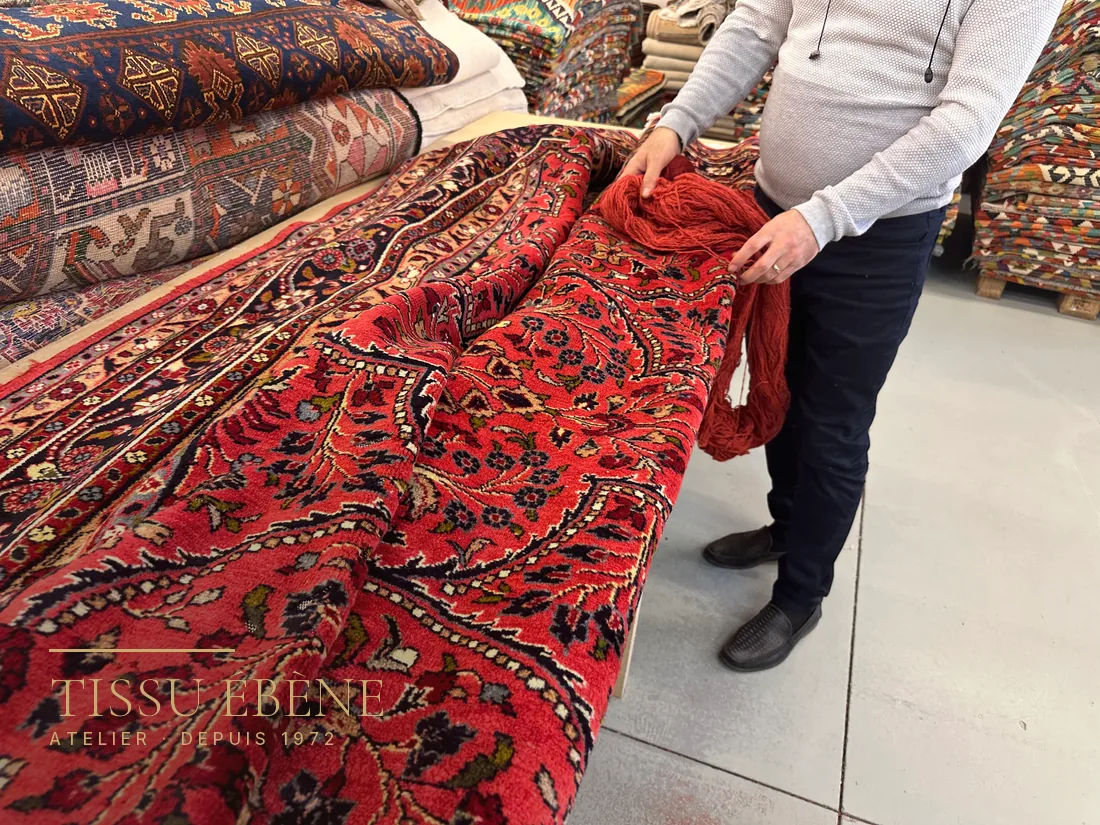Expert de Tissu Ébène comparant les laines d’un tapis à Paris, parmi les pièces de l’atelier