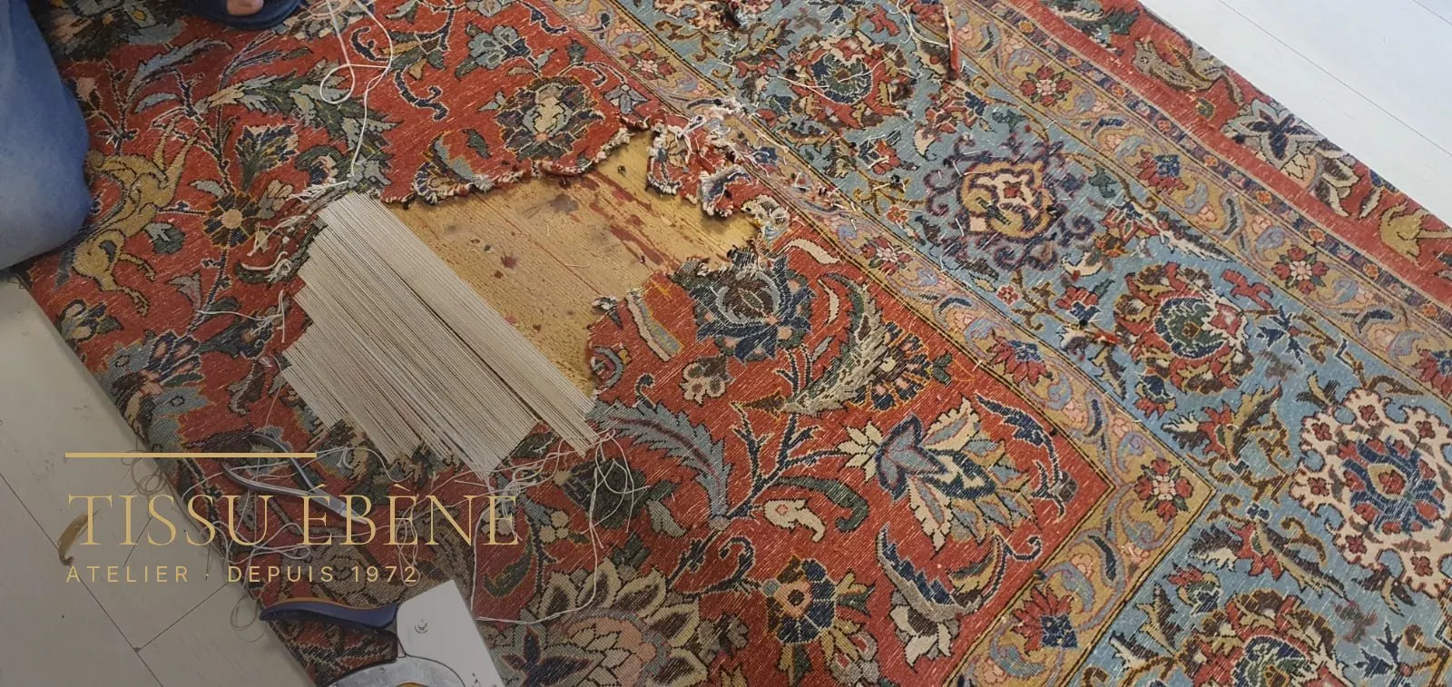 Retissage d&rsquo;un trou de tapis : fils de chaîne neufs retendus en travers de la lacune, à l&rsquo;atelier