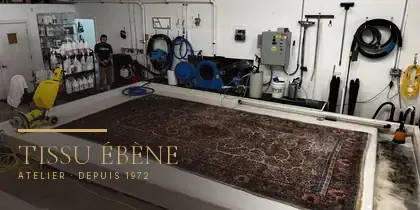 Grand tapis à décor floral étendu sur une large table d&rsquo;atelier, tuyaux et machines en arrière-plan